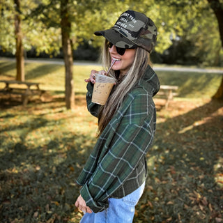 Support Your Local Mother® Trucker Hat - Camo
Woman in a park wearing a plaid jacket and camouflage cap, holding a drink.