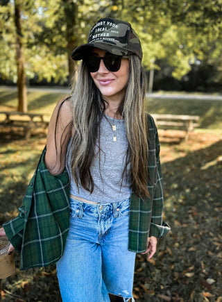 Support Your Local Mother® Trucker Hat - Camo
Woman wearing a cap, sunglasses, and plaid shirt outdoors