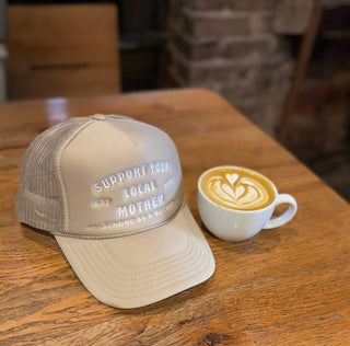 Support Your Local Mother® Trucker Hat - Tan
Beige cap with text and a cup of coffee on a wooden table