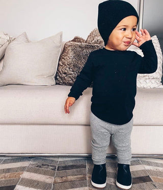 Little Bipsy Long Sleeve Pocket Tee - Black
Child wearing a black sweater and gray pants standing in front of a white couch.