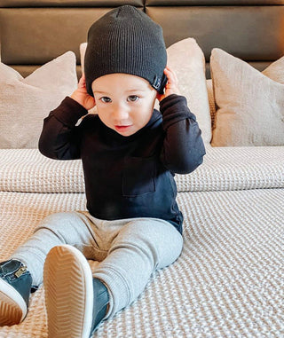 Little Bipsy Long Sleeve Pocket Tee - Black
Child wearing a black beanie and dark hoodie sitting on a beige couch.
