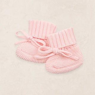 Lou Lou and Company Knit Booties - Blush
Pair of pink knitted baby booties with a bow on a light beige background