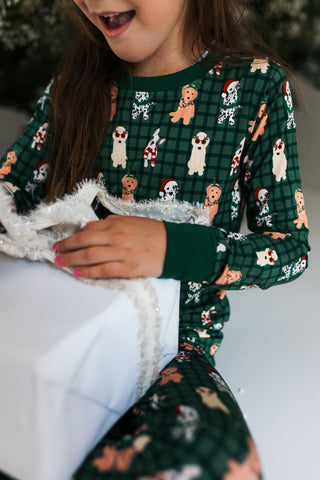 In My Jammers Christmas Pups Two Piece Set
Child wearing a green pajama set with dog pattern, sitting on a white surface.