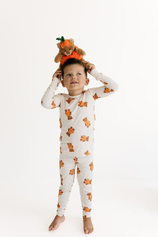 In My Jammers Two Piece Set - Gingham Little Boo Bear
A young child wearing a long-sleeve waffle-knit pajama set with an orange teddy bear pattern, standing barefoot against a white studio background while holding a small plush teddy bear on their head.