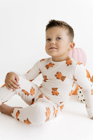 In My Jammers Two Piece Set - Gingham Little Boo BearA young child wearing a long-sleeve and matching pants pajama set with an orange teddy bear print on a white gingham background, sitting against a white background.
