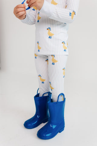 In My Jammers Two Piece Set - Striped Ducks
Child wearing duck-patterned pajamas and blue rain boots on a plain background