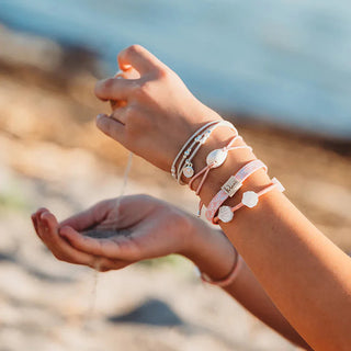 K'lani "Shimmer" Coral with Shell Hair Tie Bracelets
Person wearing multiple bracelets on a blurred beach background