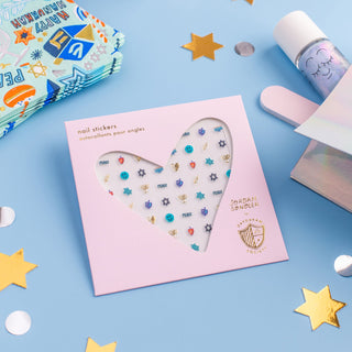 Jollity & Co Festival of Lights Nail Stickers
Nail sticker set with star designs on a pink card, surrounded by decorative items on a blue background.