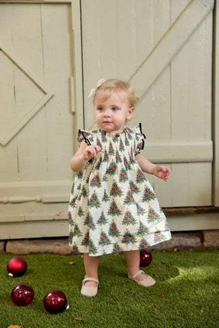 Pink Chicken Baby Girls Stevie Dress Set - Vintage Trees
Child wearing a patterned dress standing outdoors with Christmas decorations.