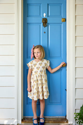 Young girl in a yellow dress standing in front of a blue door.