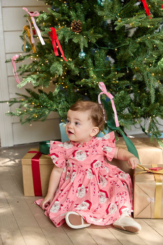 Pink Chicken Baby Girls Jennifer Dress Set - Pink Candy Cane Santa
Child in a pink dress sitting in front of a decorated Christmas tree with presents underneath.