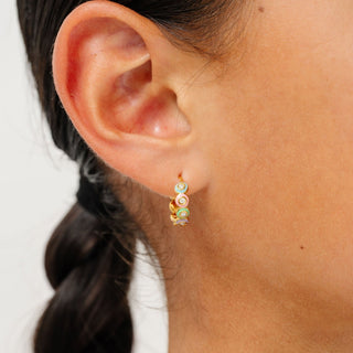 Pip Pop Post Earrings - Rainbow Enamel Hoop
A close-up of a model's ear wearing a small gold huggie hoop earring with three stacked spiral charms in pastel green, orange, and white.