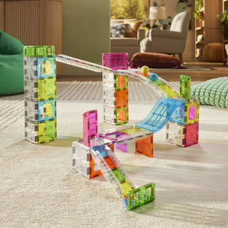 Magna-Tiles Rail Racers™ Max 80-Piece Set
Colorful magnetic building blocks on a carpeted floor with a living room in the background