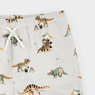 Petit Lem beach swim trunks with dinosaur print on beige fabric, perfect for kids' summer beachwear.