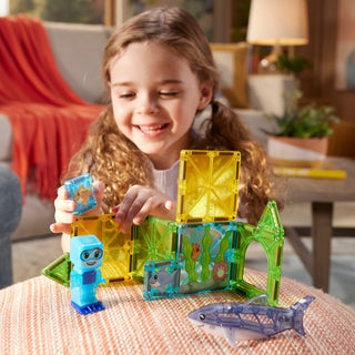 Magna-Tiles Shark Dive™ 13-Piece Set
Young girl playing with transparent building blocks in a living room setting