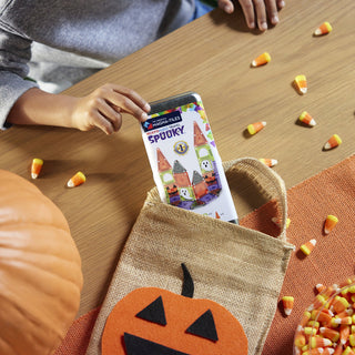 Magna-Tiles microMAGS Spooky 24-Piece Travel Set
Person holding a smartphone with a Halloween-themed app over a burlap bag with a pumpkin design, surrounded by candy corn on a wooden table.