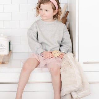 Saranoni Lush Receiving Blanket - Buttermilk
Young girl sitting on a step wearing a gray sweater and pink skirt, holding a cookie.