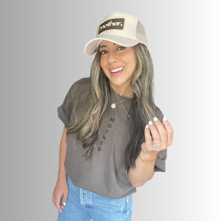 Mother Patch Trucker Hat - Sand
Woman wearing a cap and t-shirt with text, smiling against a plain background