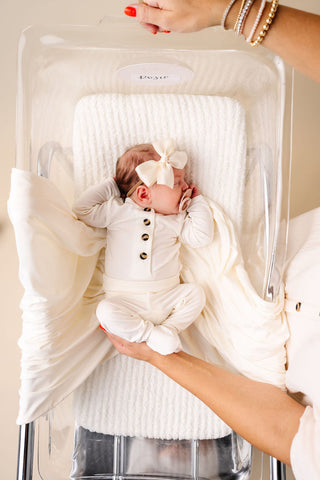 Lou Lou and Company Top and Bottoms - Finley
Baby in a white outfit with a bow lying in a bassinet.