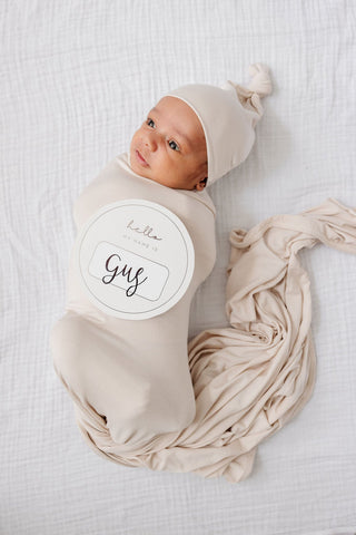 Lou Lou and Company Swaddle Blanket - Winnie
Newborn baby wrapped in beige swaddle with a hat, lying on a white textured surface.