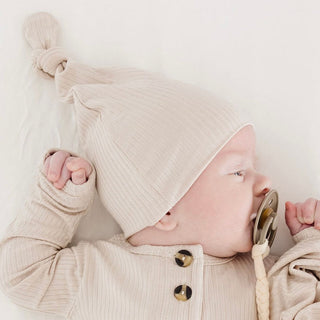 Lou Lou and Company Ribbed Top Knot Hat - Cove
Baby wearing a beige knitted hat and holding a pacifier with a white background