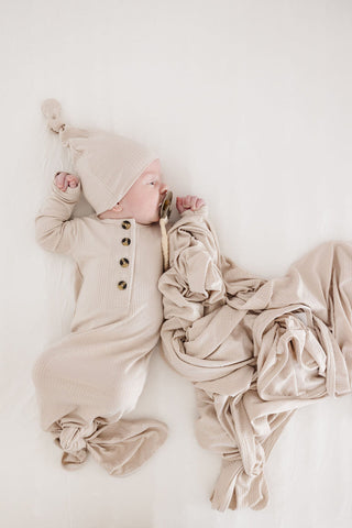 Lou Lou and Company Ribbed Swaddle Blanket - Cove
Newborn baby in beige outfit and hat lying on a white surface with a beige blanket.