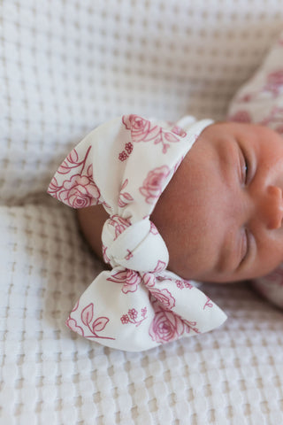 In My Jammers Blush Rose Garden Headband
Newborn baby with a floral headband on a soft textured blanket