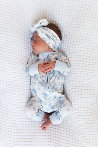 In My Jammers Blue Rose Garden Headband
Newborn baby in floral outfit and headband lying on a textured surface
