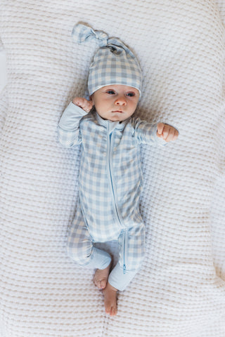 In My Jammers Blue Gingham Zipper Romper
Baby in blue checkered outfit and hat lying on a textured white blanket