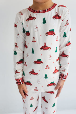 In My Jammers Red Holly Jolly Cruisers Two Piece Set
Child wearing a Christmas-themed pajama set with red trucks and trees on a white background