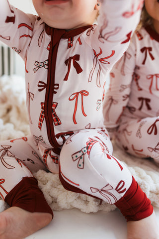 In My Jammers Merry Little Bows Zipper Romper
Children wearing pajamas with red bows on a white surface