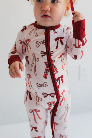 In My Jammers Merry Little Bows Zipper Romper
Baby wearing a white onesie with red bow patterns on a plain background