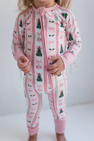 In My Jammers Pinkmas Zipper Romper 
Child wearing a pink onesie with Christmas tree and bow pattern on a white background
