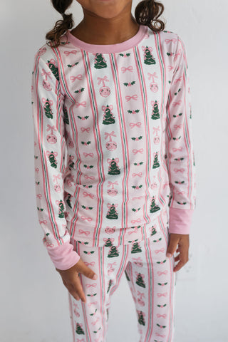 In My Jammers Pinkmas Two Piece Set 
Child wearing a pajama set with Christmas tree and bow pattern on a plain background