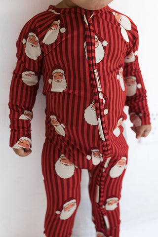Red and white striped pajama set with Santa Claus faces on a child, against a plain background.
