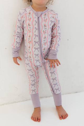 In My Jammers Zipper Romper - Purple Amelia Bow
Child wearing a purple onesie with bow pattern on a white background