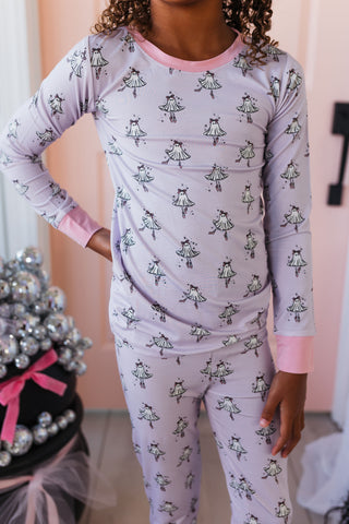 In My Jammers Ballerina Ghost Two Piece Set Child wearing a purple pajama set with a pattern of small figures, standing in a room.