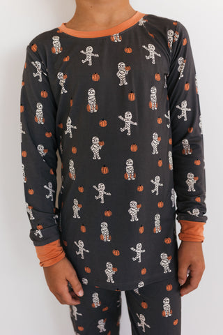 In My Jammers Mummy Two Piece Set Child wearing black pajamas with skeleton and pumpkin pattern on a white background
