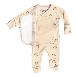 Bonsie Footie - Little Wishes
A baby footed sleeper set in a warm cream-beige color, featuring a repeating pattern of small brown and pastel rainbow motifs. The set includes a long-sleeve top with an asymmetrical snap closure, a large front bib panel, and matching footed pants with a brand logo on the ankle.