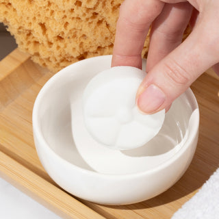 The Lavish Goat Shower Steamers Box - Essence: Eucalyptus
Hand holding a white sphere over a small white dish with a sponge in the background on a wooden surface.