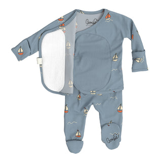 Bonsie Footie - Ahoy Baby/
A baby footed sleeper set in dusty blue, featuring a long-sleeve top with an open snap closure showing a white fleece lining, and matching footed pants with a sailboat print. The brand name 'Bourdy' is visible on the inner neck label and printed on the leg.
