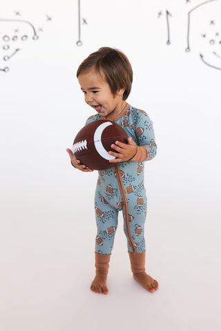 In My Jammers Green Football Zipper Romper
Child wearing a patterned onesie holding a football against a white background