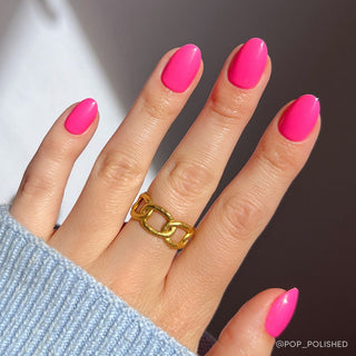 Glamnetic Press-On Nails Short Round - Hot Pink
Hand with pink nails and a gold ring on a dark background