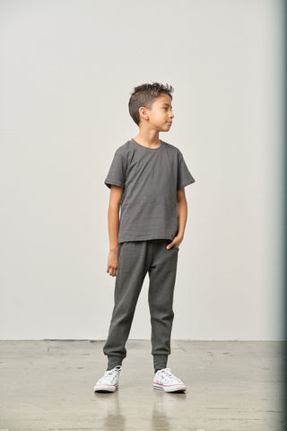 Little Bipsy Elevated Tee - Shadow
Young boy wearing a gray t-shirt and pants standing against a plain white wall.