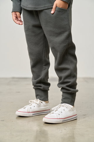 Little Bipsy Waffle Jogger - Shadow
Person wearing gray sweatpants and white sneakers on a plain background