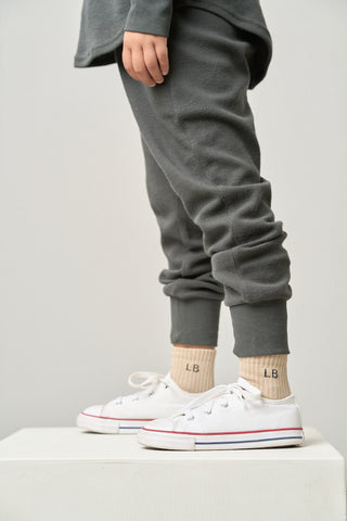 Little Bipsy Waffle Jogger - Shadow
Person wearing gray sweatpants and white sneakers with tan socks on a light gray background