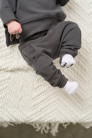 Little Bipsy Jogger - Shadow
Child wearing dark gray pants and a matching top on a textured white surface