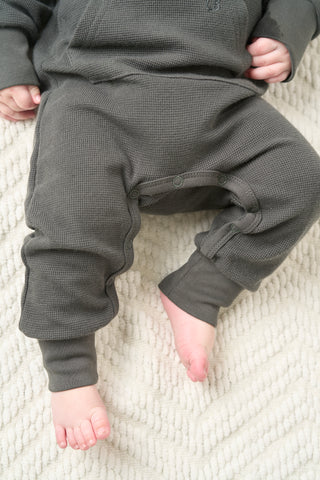Little Bipsy Waffle Romper - Shadow
Child wearing dark gray pajama pants on a light textured surface