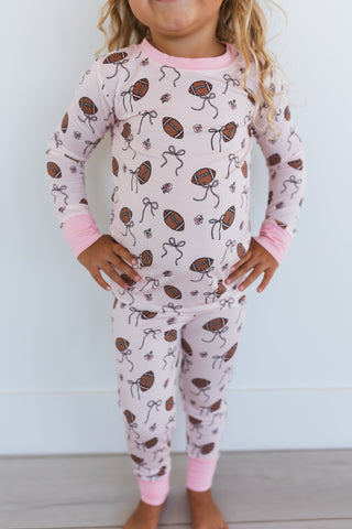In My Jammers Blush Football Two Piece Set
Child wearing pajamas with football and bow pattern on a white background
