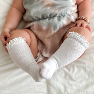 Little Stocking Co Lace Top Knee High Socks - White
Baby wearing white socks with lace tops on a soft surface